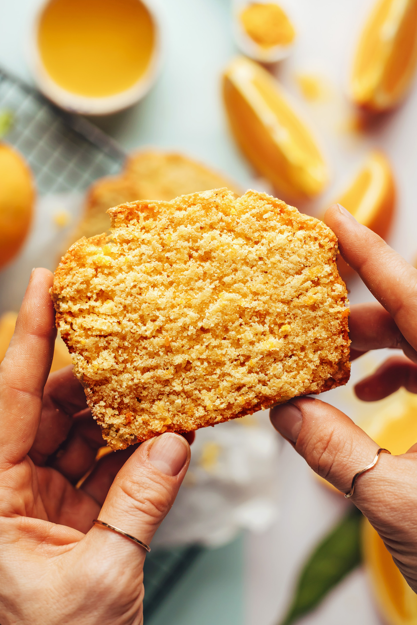 Close-up shot of hands holding a slice of orange almond cake to show the moist texture