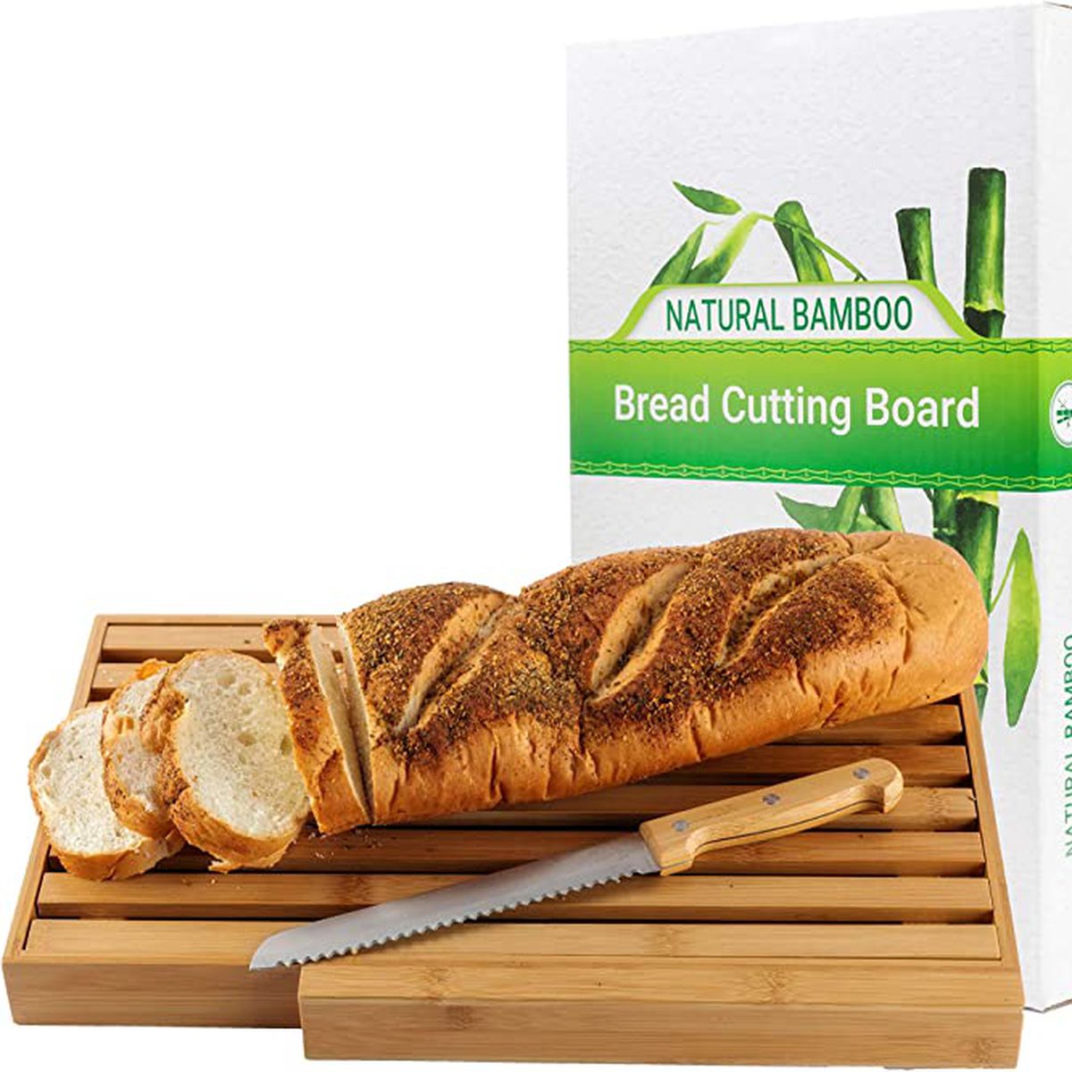 A slotted bread cutting board with a bread knife and loaf of bread