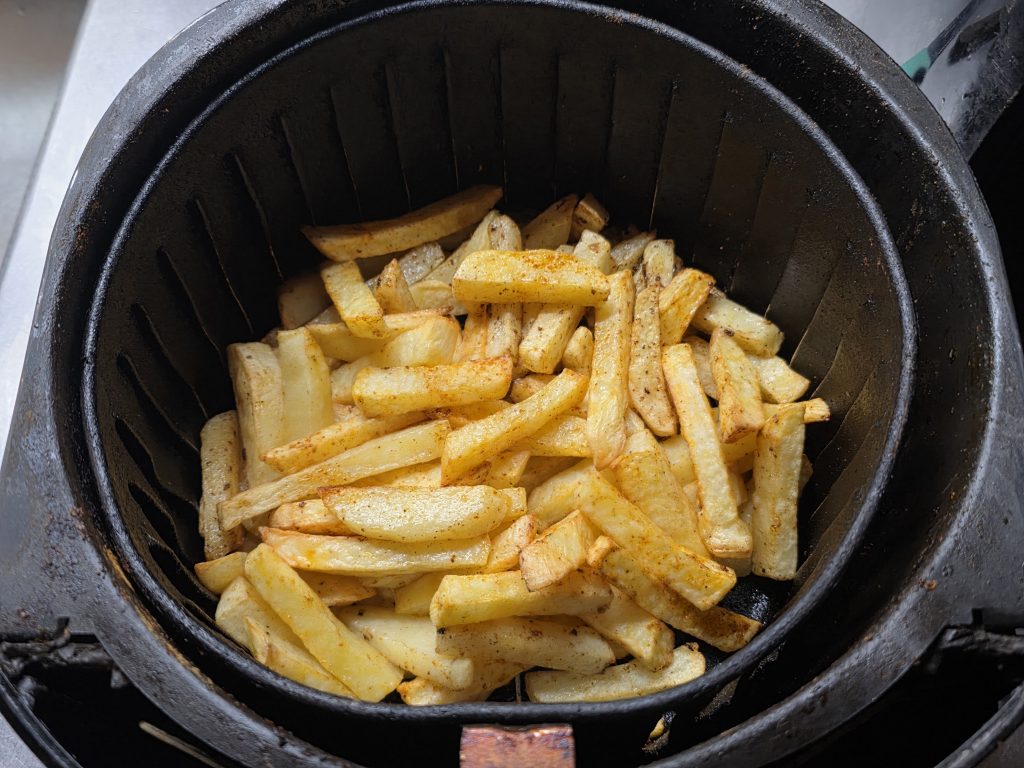 Basket of french fries lifted out of hot fryer oil