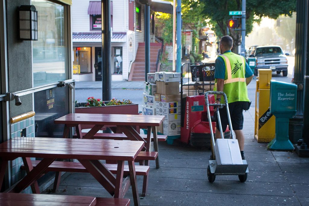 A delivery driver wheeling cases on a hand truck to a restaurant